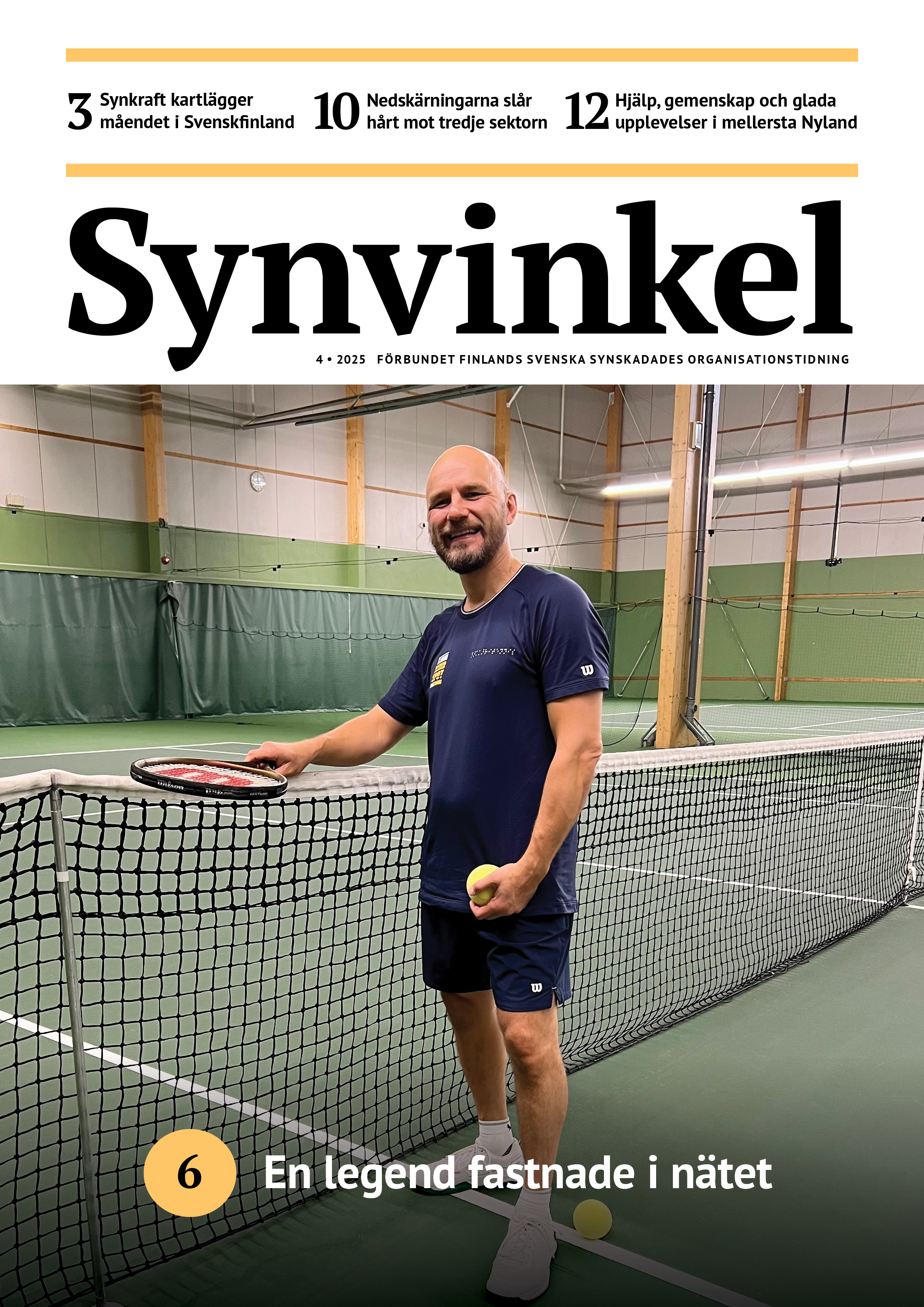 En leende man i mörkblå t-skjorta, shorts och vita tennisskor står på en tennisplan inomhus. Han håller racketen i höger hand, vilande mot nätet, och en stor gul blindtennisboll i vänster hand.