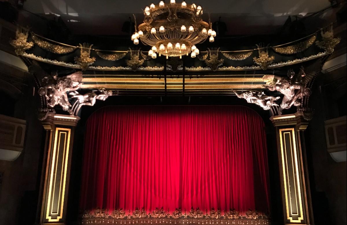 Bild på teaterscen med guldkrona i taket och vinröd sammetsridå.