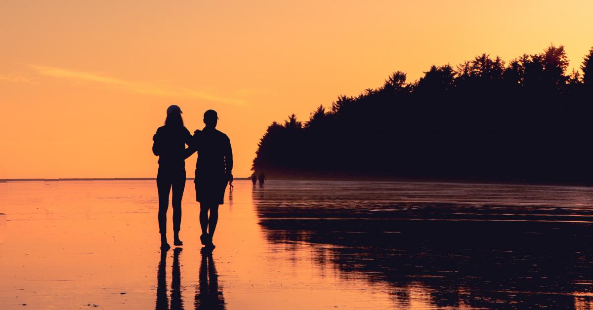 Siluetter av två personer promenerande på en strand.