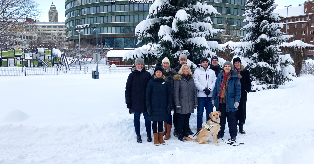 FSS:s personal, inklusive ledarhunden Palo står uppställda framför snötyngda granar i Hagnäs i Helsingfors.