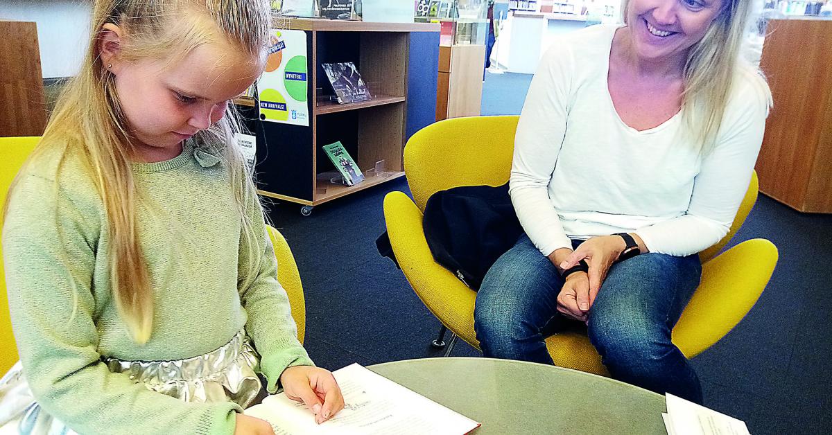 Sexåriga Charlotta Saari testar ett förstoringskort i Åbo stadsbibliotek. Mamma Katarina Katajainen sitter bredvid.