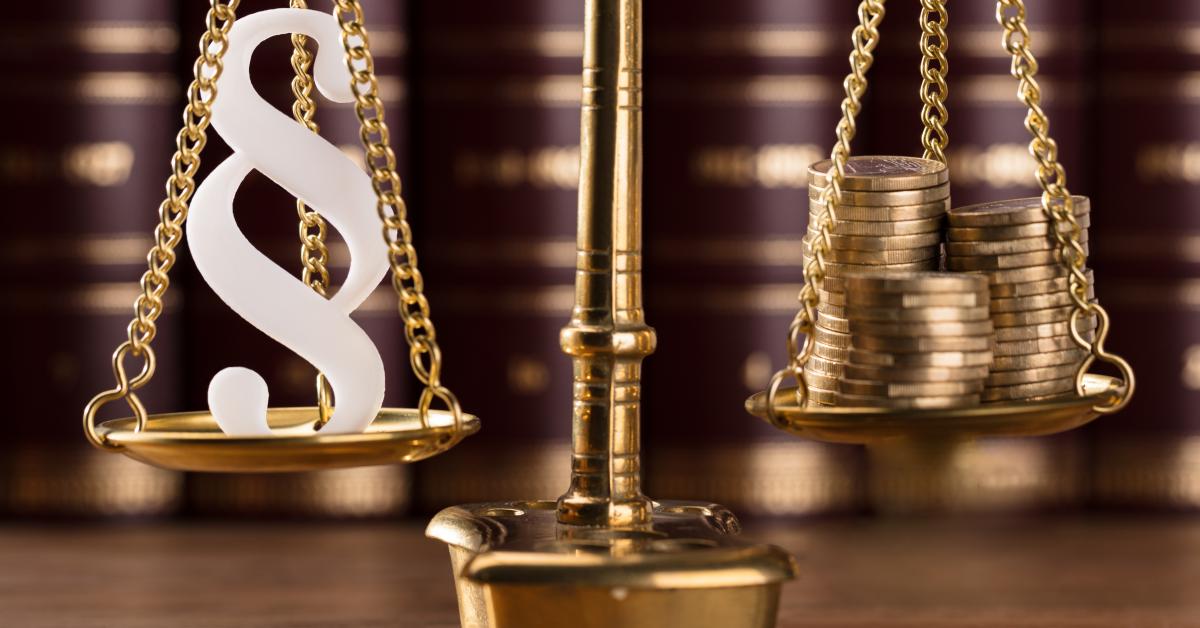 En gyllene våg med 2 vågskålar. Iden ena en lagparagraf och i den andra pengar.