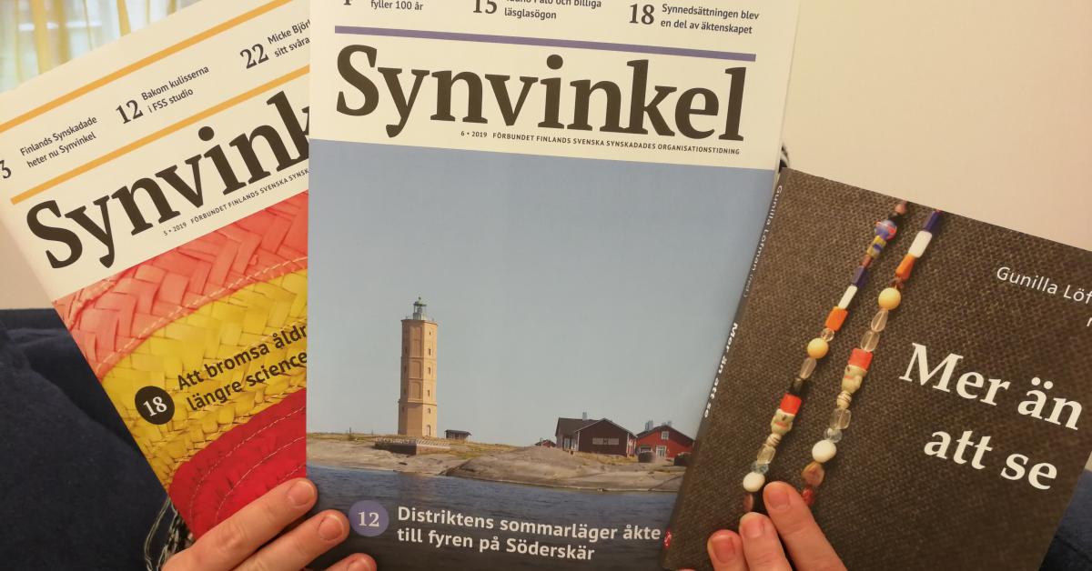 Händer håller uppe två exemplar av tidningen Synvinkel och boken Mer än att se. Pärmen på boken: ett färggrant pärlhalsband mot en mörk bakkgrund.