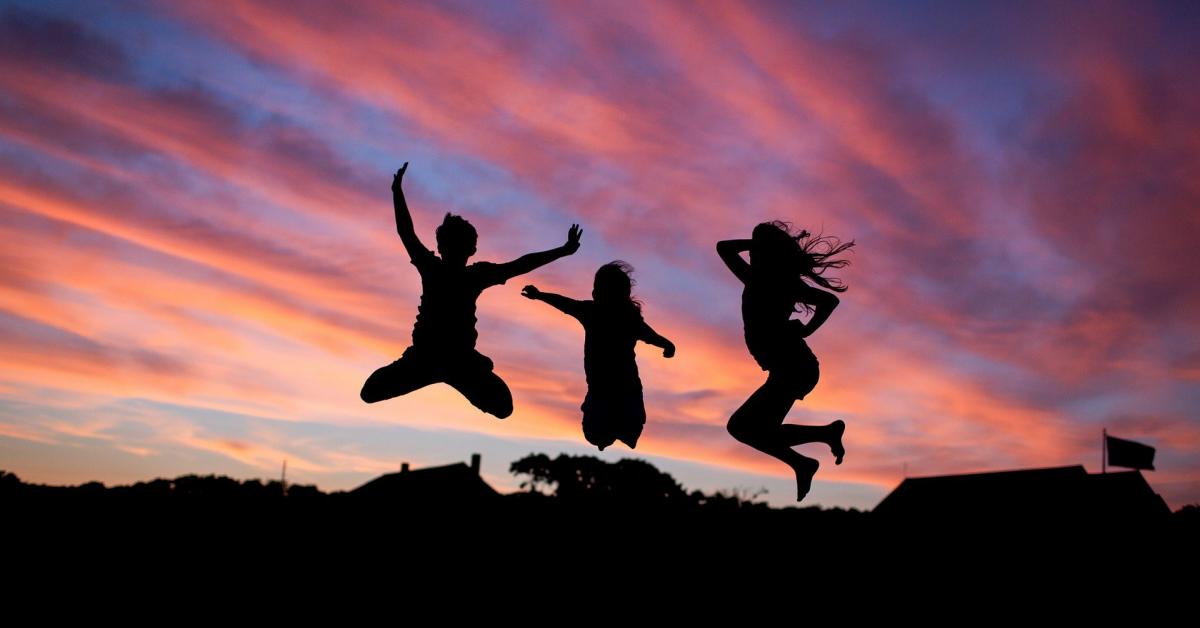 Siluetter av tre personer hoppar glatt i solnedgång.