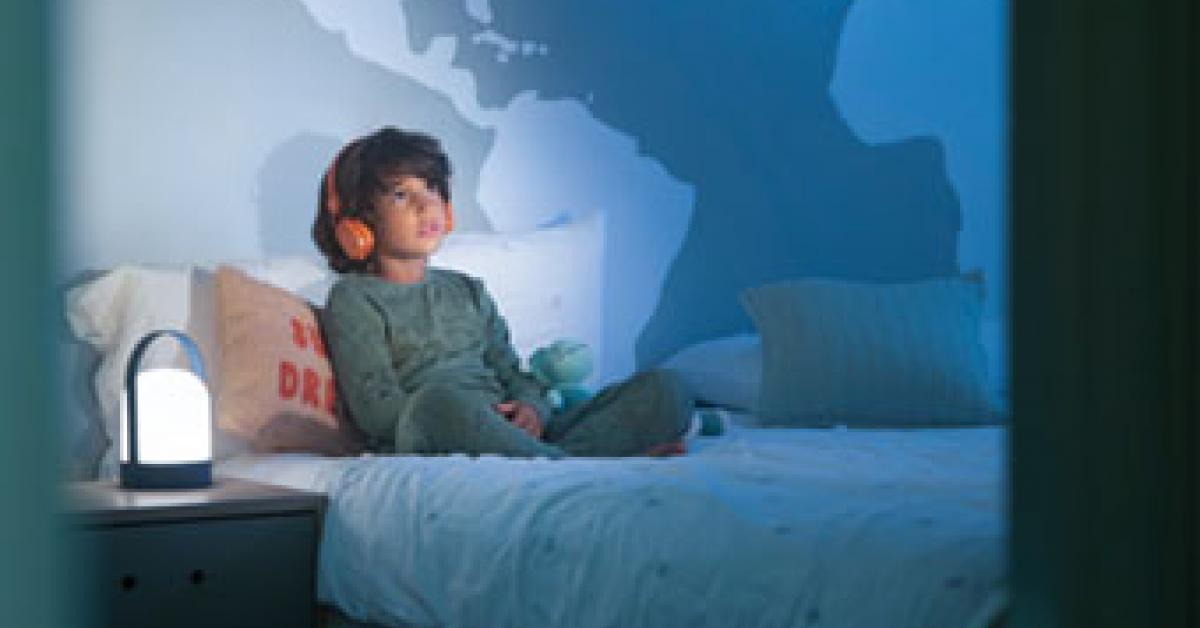 En pojke i skolåldern sitter på sin säng och lyssnar på en ljudbok i hörlurarna. Det är kväll,