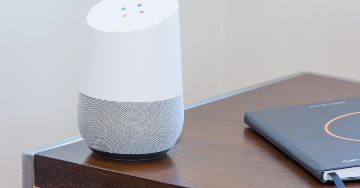 Vitgrå google home-smarthögtalare på ett bord bredvid ett anteckningshäfte.